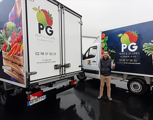 Homme devant deux camions floqués PG Fruits